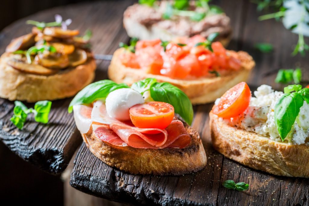 Verschieden belegte Crostini mit Schinken, Mozzarella, Tomaten, Ricotta und Basilikum