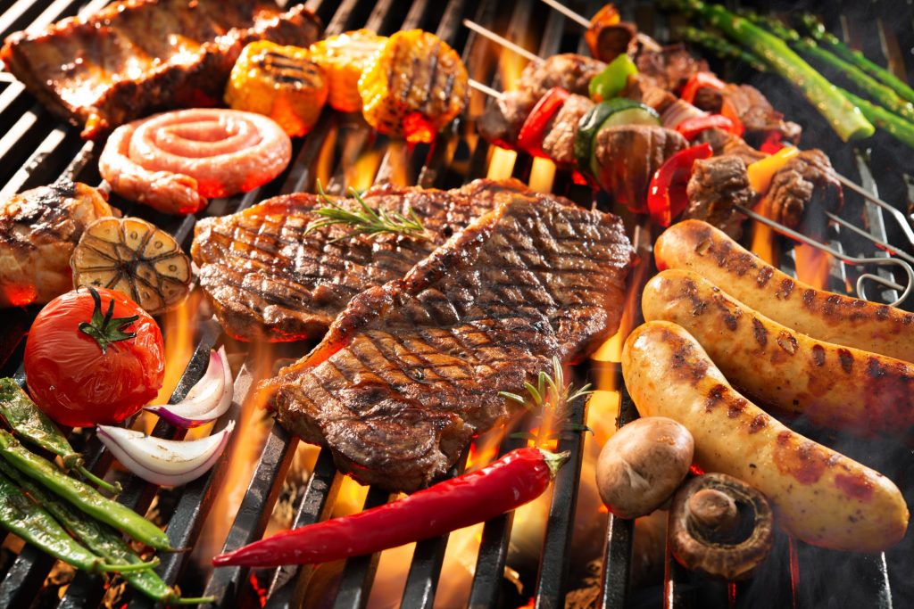 Steaks, Bratwürste, Fleischspieße und Gemüse auf einem offenen Grill.
