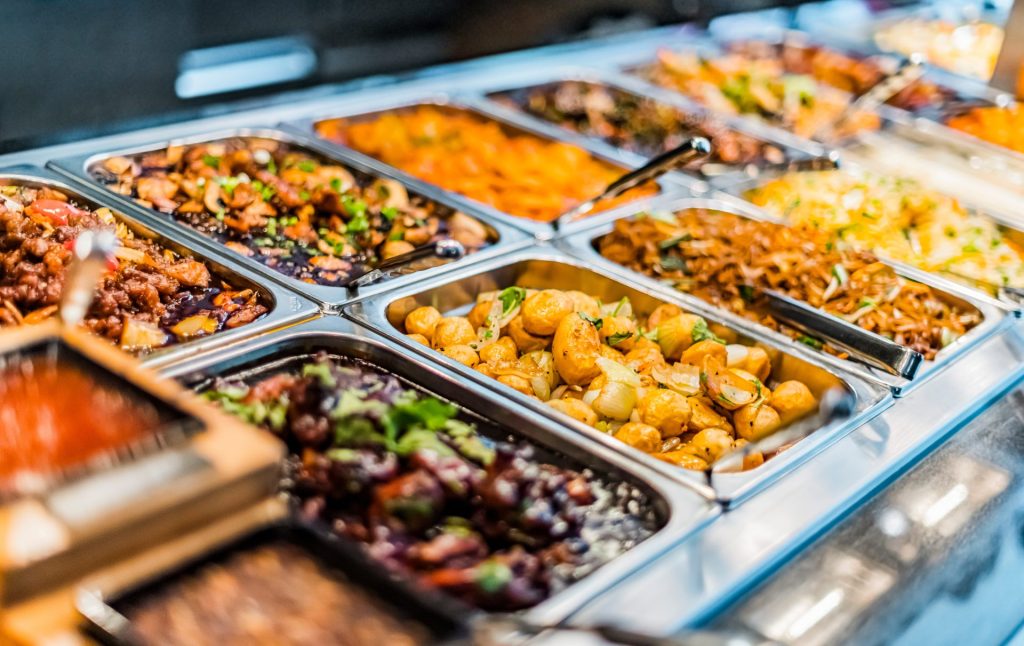 Buffet mit verschiedenen Fleisch-, Kartoffel-, Gemüse- und Nudelgerichten in Edelstahlbehältern.